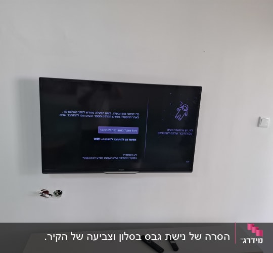 טלוויזיה מותקנת על קיר לבן מעל פתחי צנרת וחשמל בקיר